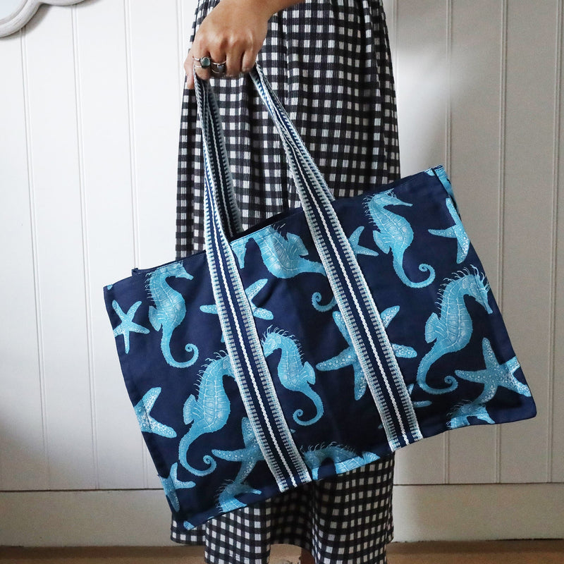 Seahorse and Starfish decorated Tote bag in a cotton and linen mix with large braided handles being swung by a woman so you can see the size.Behind her is a wave mirror on the wall