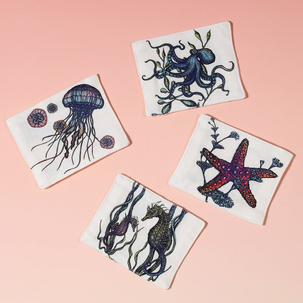 Cotton and linen mix white fabric rectangular coaster.Design is on both sides hand drawn illustrations set of four- one Jellyfish ,octopus, starfish and one with a seahorse design in various colours.