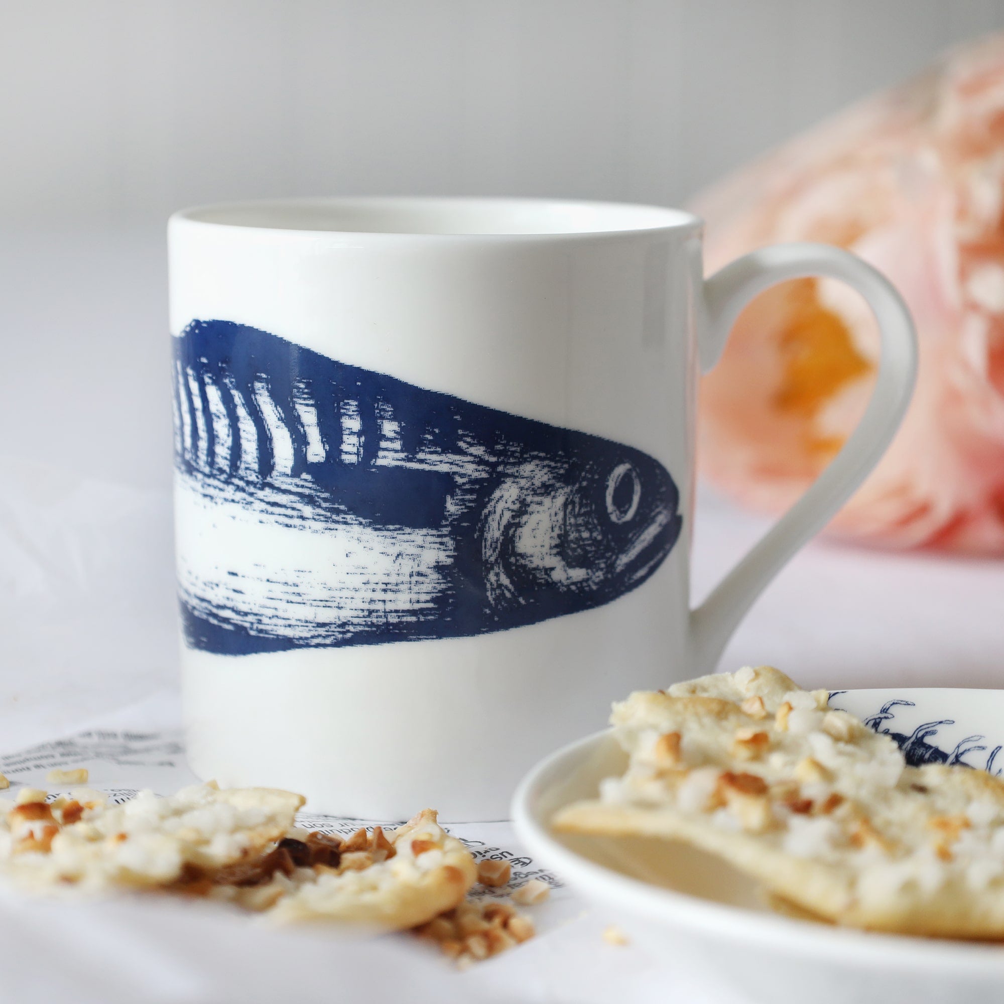 Blue & white bone china mackerel mug on table with biscuits & flowers.