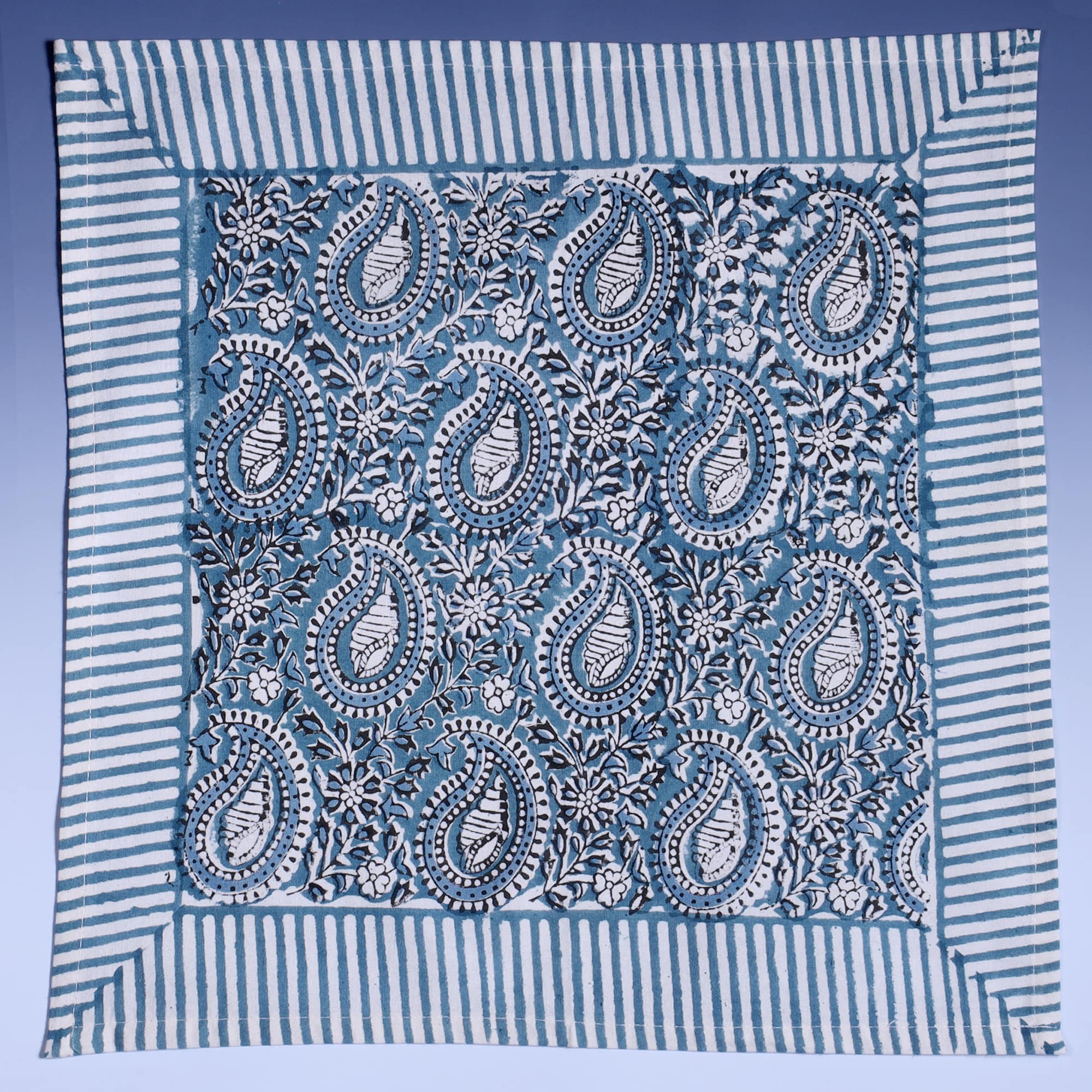 Azure Paisley Shell napkin which is Hand block printed fabric in a soft blue, the print is a repeat paisley with a shell theme throughout with swirling flowers, blue striped finished edge.