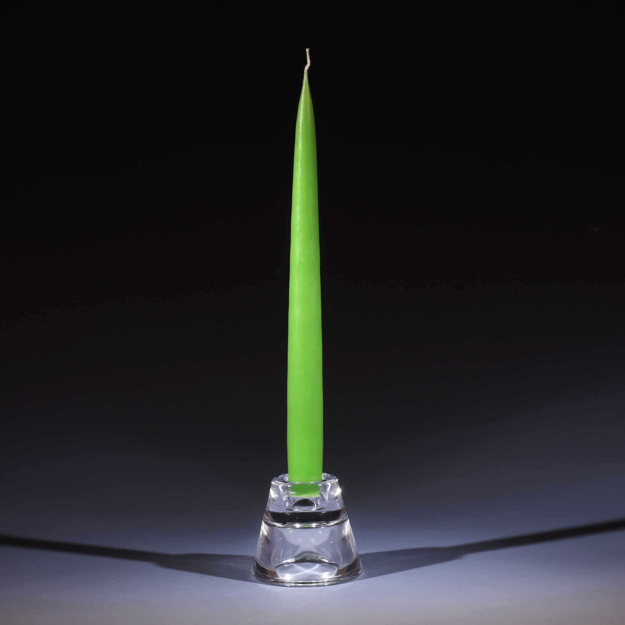 spring green tapered dinner candle in a small glass candle holder on an ombre blue background