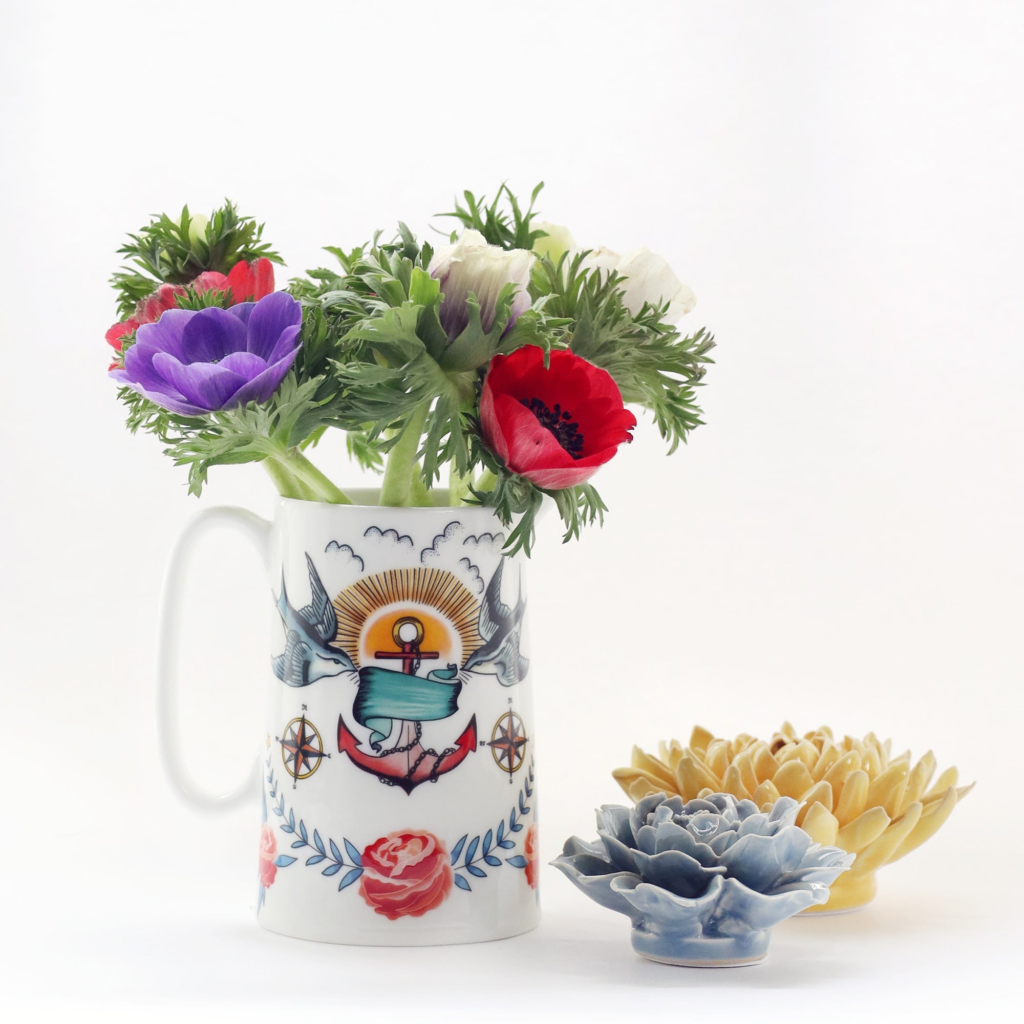 White bone china jug with brightly coloured tattoo inspired design of swallows, anchor and roses with red, white and purple anemones in it. The are 2 ceramic flowers next to it.