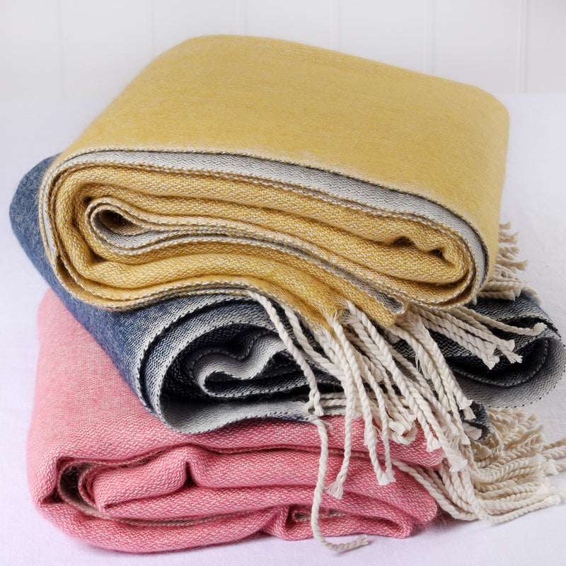pile of 3 brushed reversible throws in pink, mustard and navy on top of each other on a white background