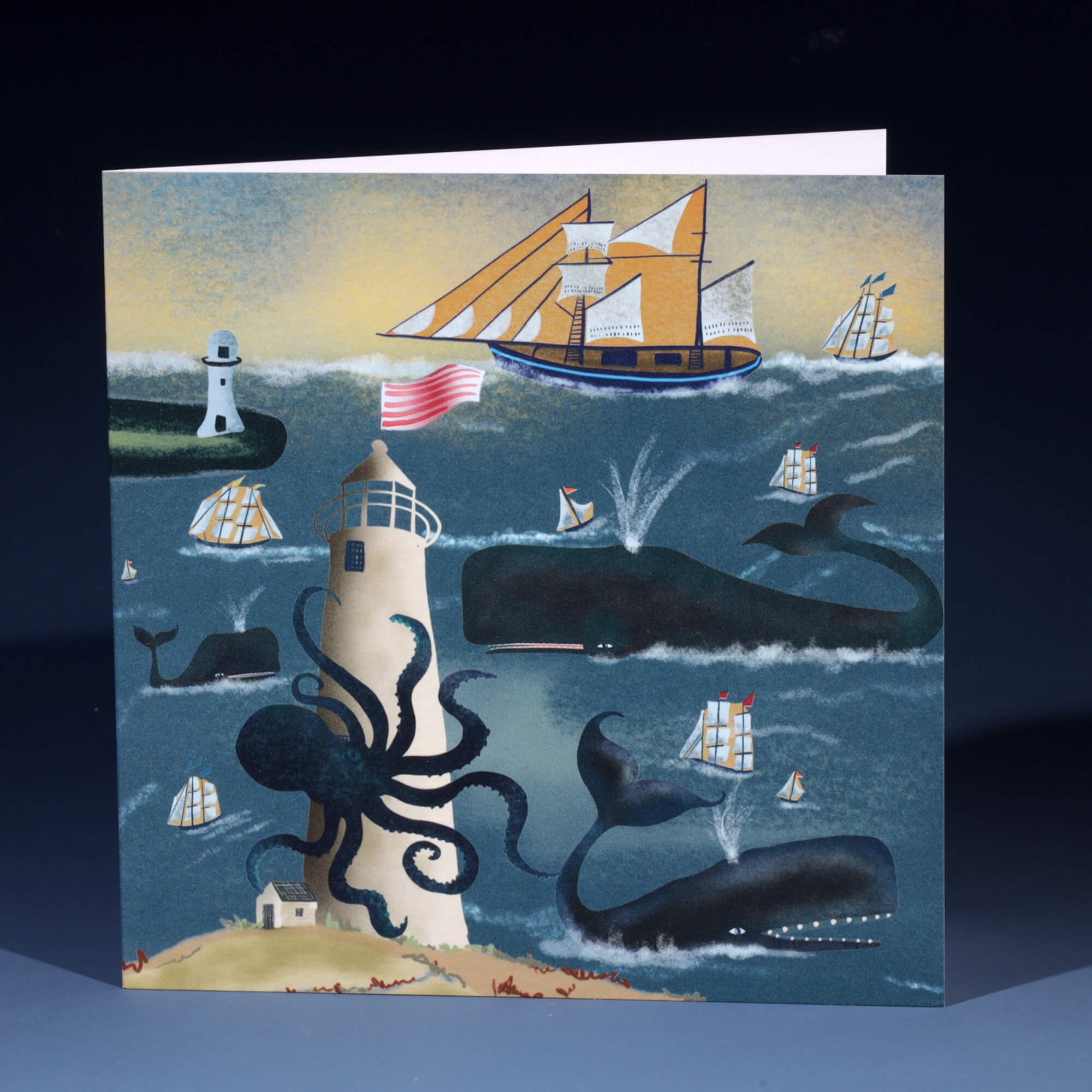 A nautical-themed greeting card featuring an illustration of whales, ships, and a lighthouse. An octopus wraps its tentacles around the lighthouse, while large whales swim nearby, spouting water. Several sailboats and ships, including a large one with orange sails and an American flag, navigate the waves. The card has a whimsical and adventurous atmosphere, with muted blue and yellow tones.