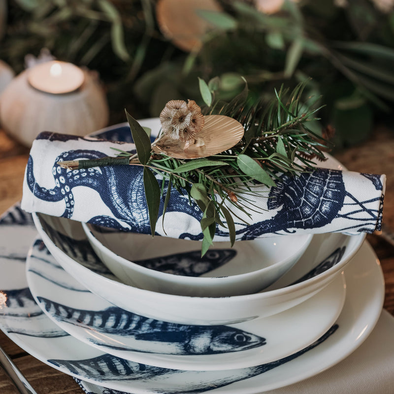 Close up of a pasta bowl in Bone China in our Classic range in Navy and white in the Mackerel design,placed on a matching dinner plate and has a smaller bowl placed inside.All are on a table setting and the table is decorated with foliage and candle holders.Placed on top of the bowls is a rolled up napkin