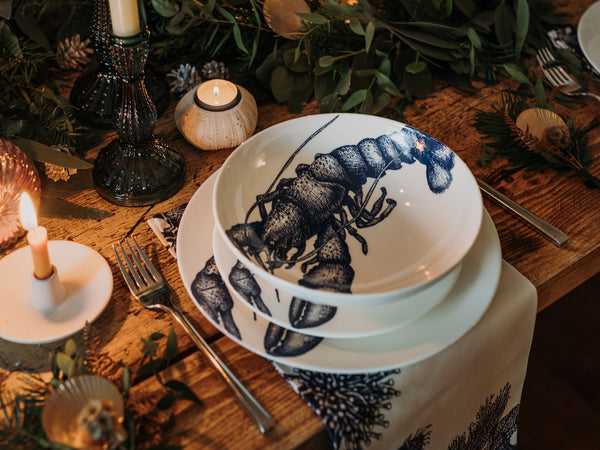 Pasta bowl in Bone China in our Classic range in Navy and white in the Lobster design,placed on a matching dinner plate and has a smaller bowl placed inside.All are on a table setting and the table is decorated with foliage and candle holders