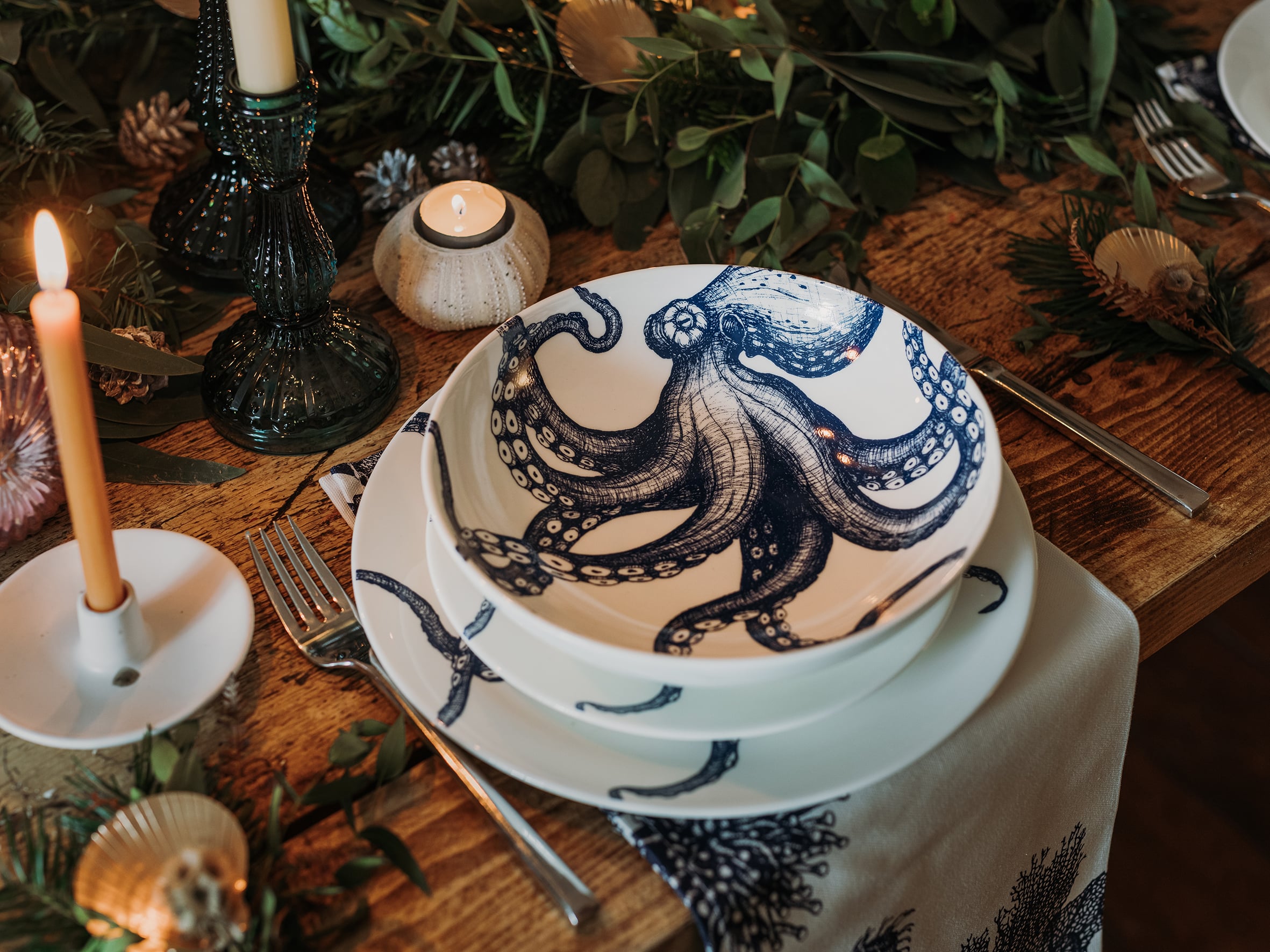 Pasta bowl in Bone China in our Classic range in Navy and white in the Octopus design,placed on a matching dinner plate..All are on a table setting and the table is decorated with foliage and candle holders