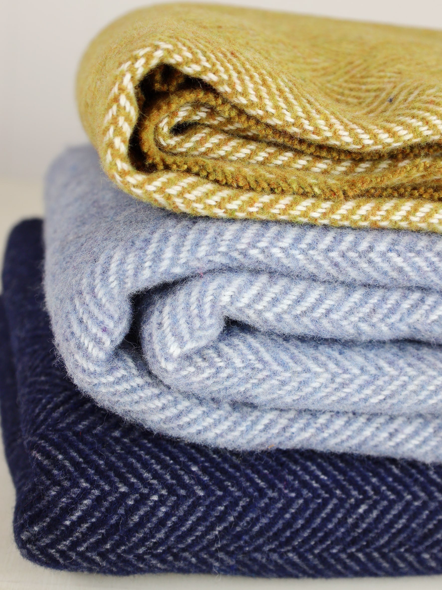 Cashmere Throw Dark Navy Herringbone at the bottom of a pile of three cashmere throws,Navy,Baby blue and Mustard.