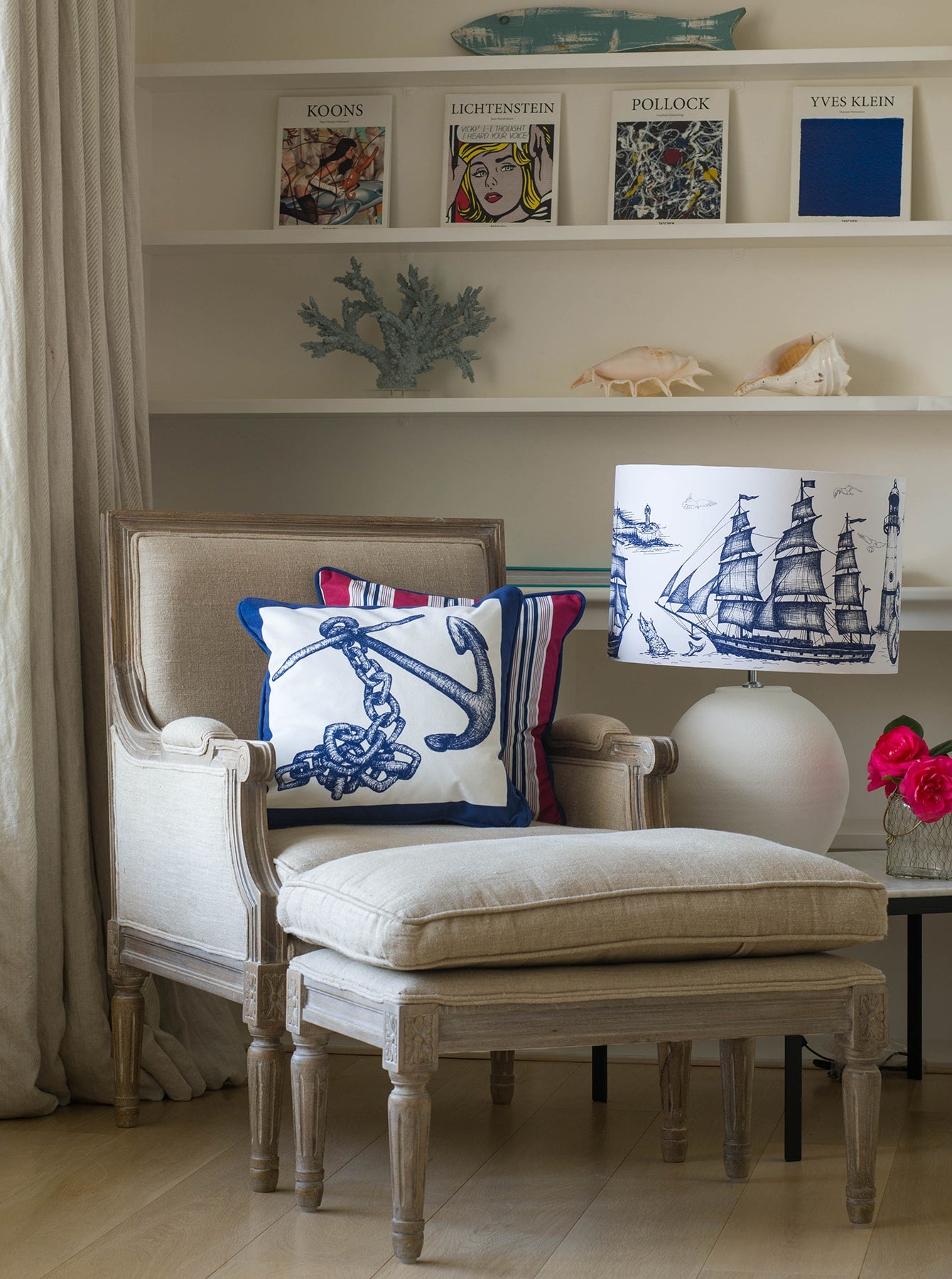 Our Classic Navy Maritime design on a white background on a lampbase on a side table next to a chair and matching footstool.Behind the chair is a bookcase with art books, coral and shells on the shelves