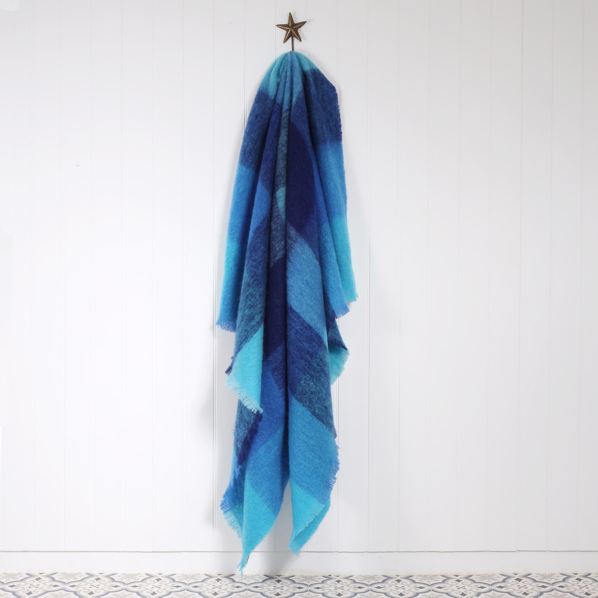 Mohair Aqua Blue Check throw hanging from a starfish hook against a white tongue and grooved wall
