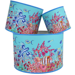 Coral Bay design lampshades in Turquoise with blue trim,with various brightly coloured fish swimming amongst the seaweed.The lampshades are shown in a stack of three showing all three sizes.