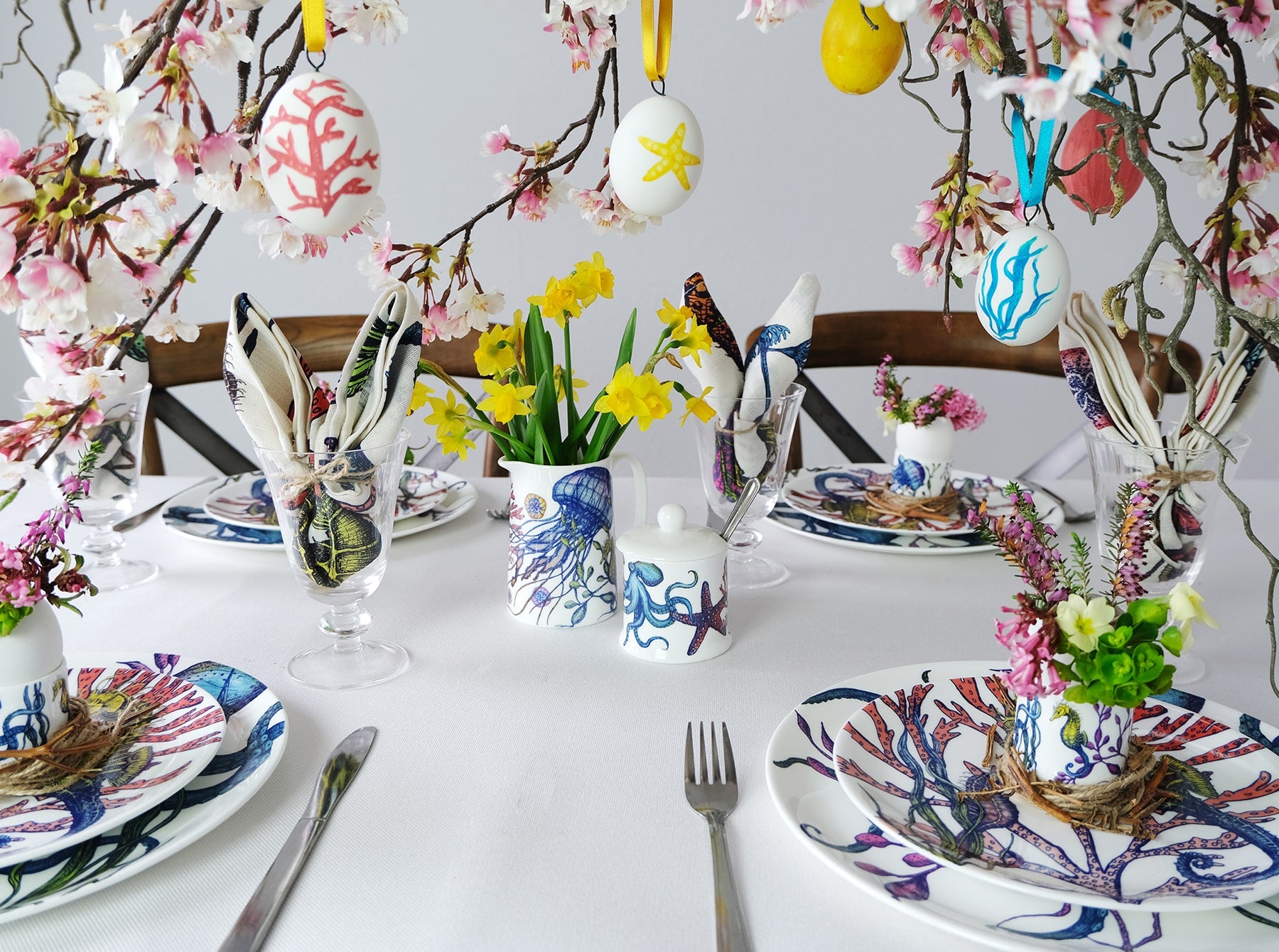 Table setting of the Reef tableware,each place has a Reef Dinner plate,side plate and an egg cup.Also on the table is a reef jug and a decorative birds nest,hanging over the table are springtime blossoms with decorative eggs