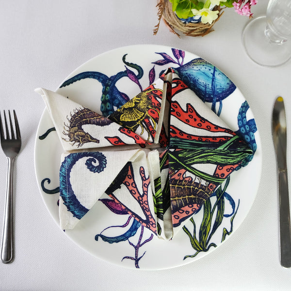 Bone China White plate with hand drawn illustration our Octopus Reef in various colours with a folded Reef napkin in the shape of a fish