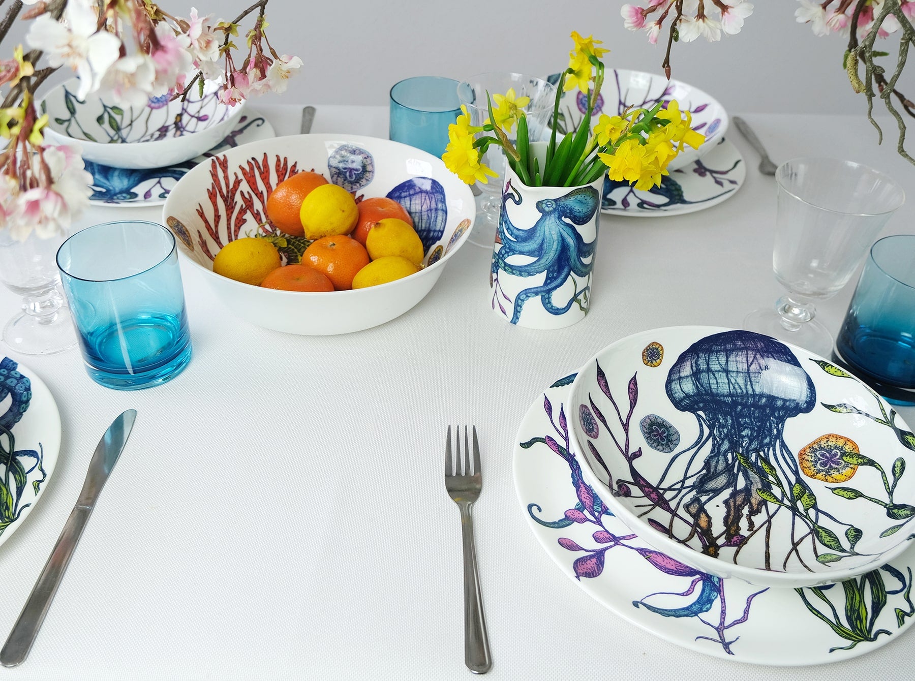 Pasta bowl in Bone China in our Reef range in Navy and white in the brightly coloured Jellyfish design,placed on a Reef Octopus plate on a table.Next to this is are other pieces from the Reef range with brightly coloured fruit and daffodils in a vase.