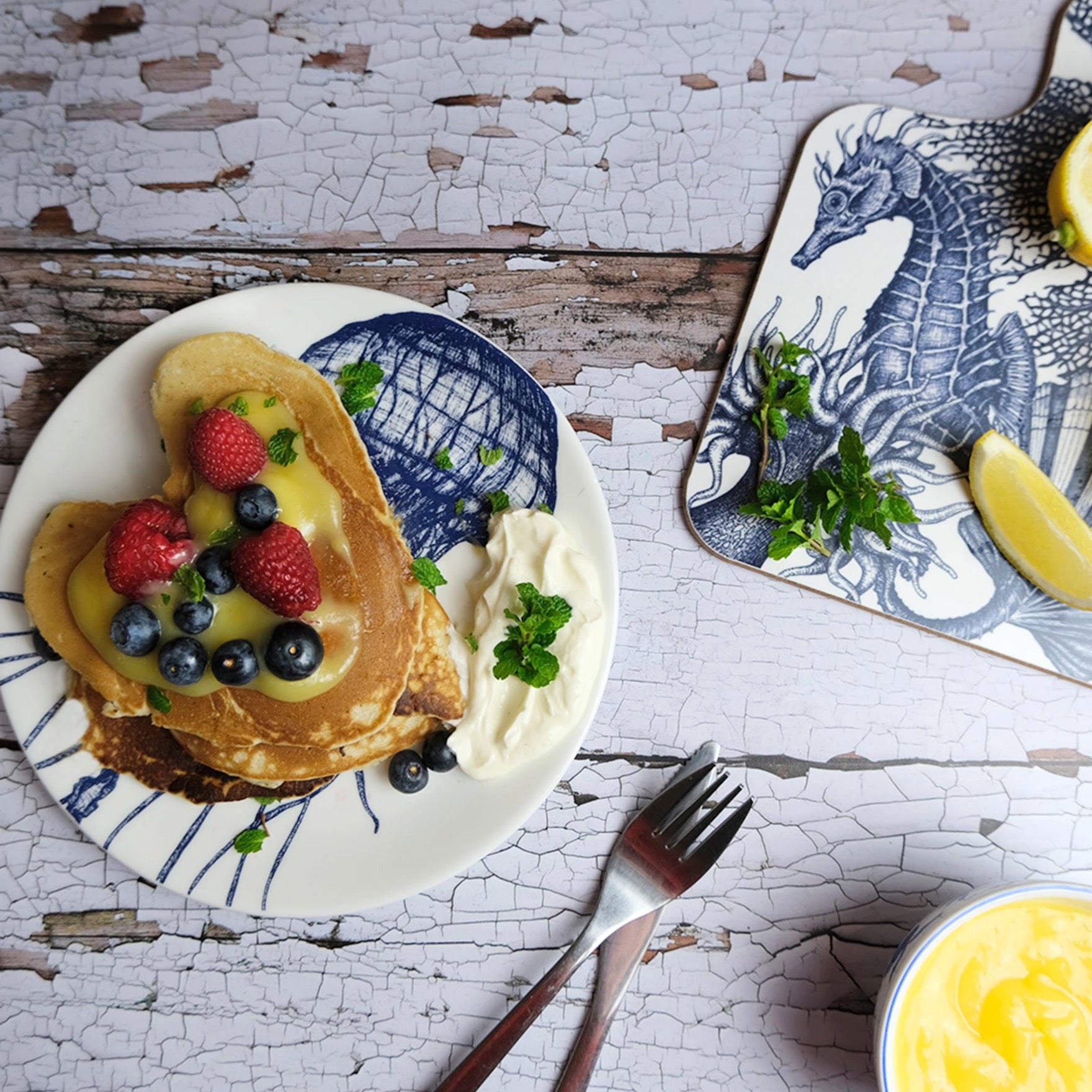 Bone China Jellyfish side plate with homemade pancakes covered with fruit. Next to the side plate is our seahorse chopping board with lemons