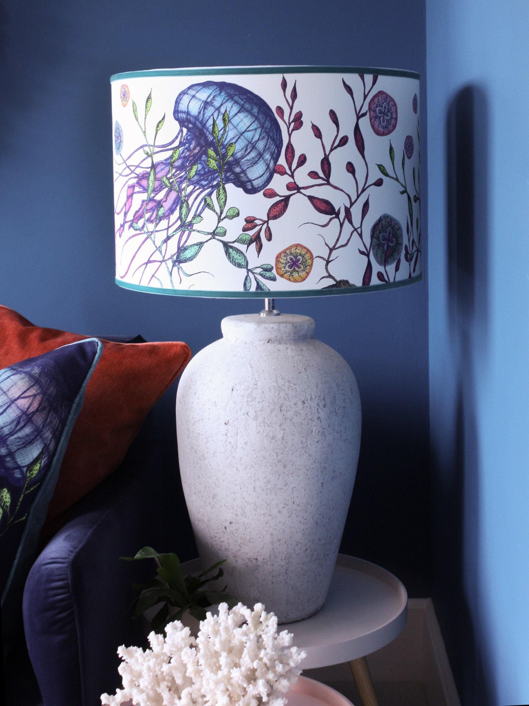 Canyons Reef White Lampshade With Jellyfish Design on a white lampbase ona small table next to a navy sofa.