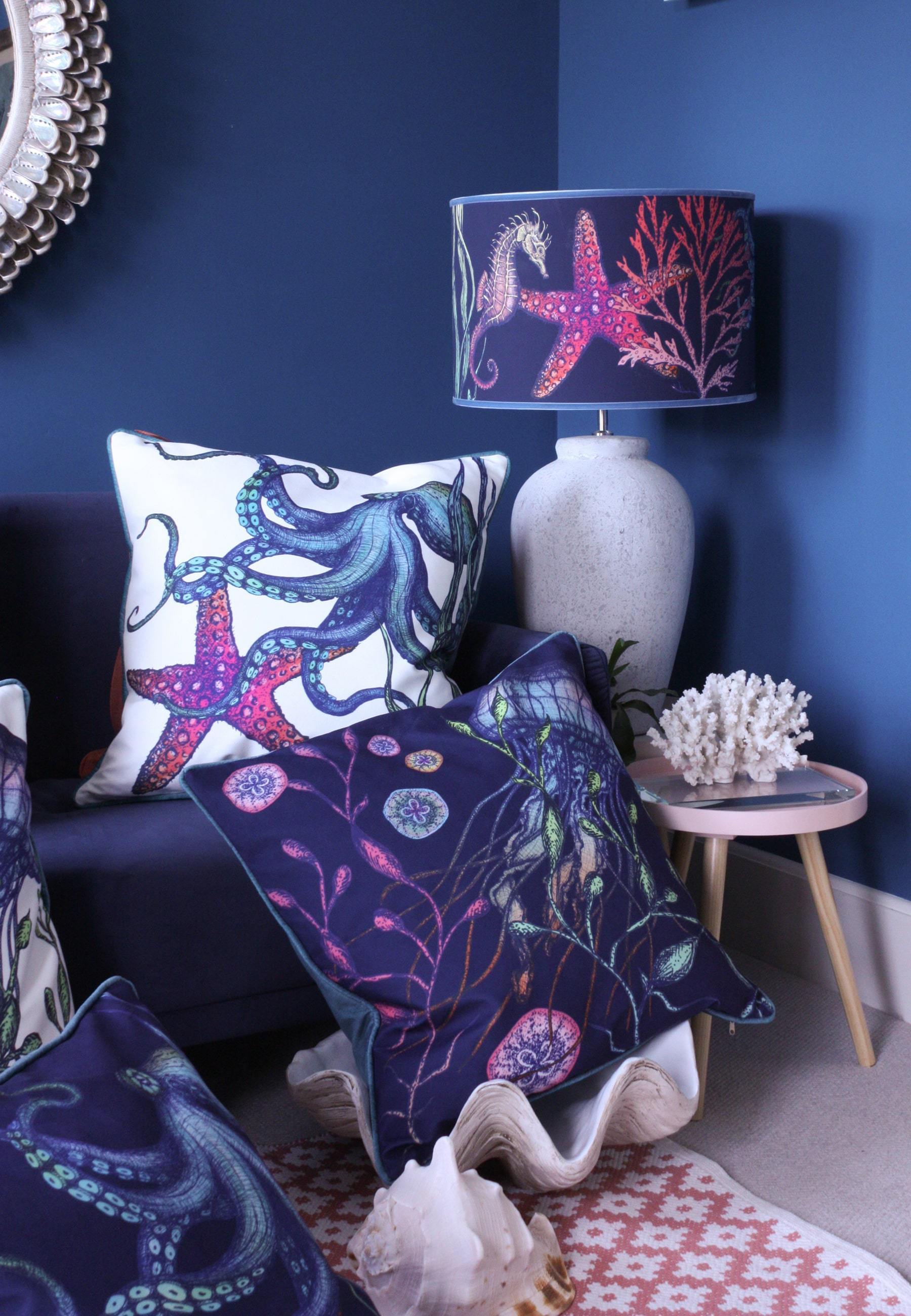 Rainbow Reef Navy Shade With Octopus,Seahorse,Starfish and Seaweed Design in bright colours on a white lampbase next to a navy sofa covered in our Reef cushions.