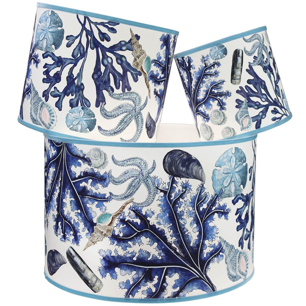 Rockpool Off White Shade With Shells,Seaweed,Sand dollars and Starfish Design in blues/browns with a blue trim on the edge of the shade.The lampshades are shown in a stack of three showing all three sizes.