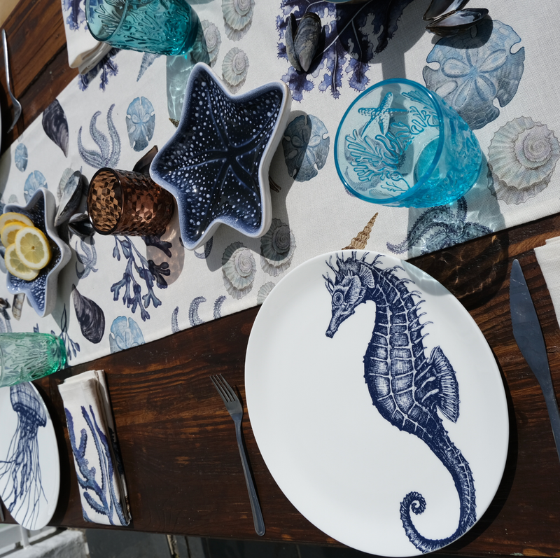 Coloured tumblers with embossed sea creatures in the glass,all set on a beachcomber tablecloth surrounded by place settings in our classic china range