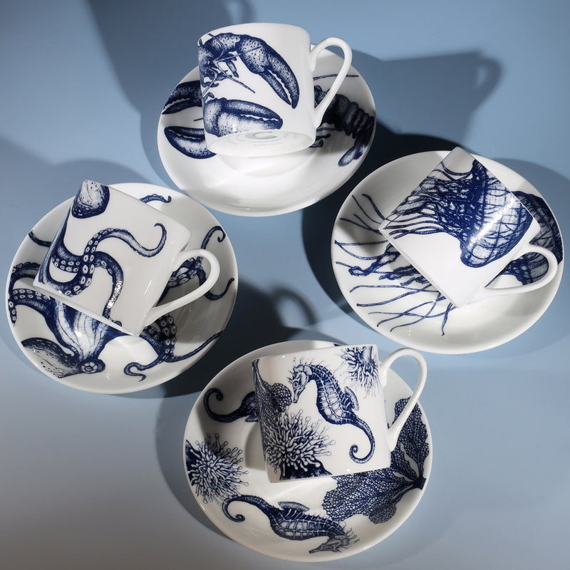Four Bone China white espresso cups in hand drawn illustrations in our Octopus,Seahorse,Jellyfish and the Lobster designs in Navy with matching saucers.Saucers are arranged in a square with the cups lying on their sides on the saucers