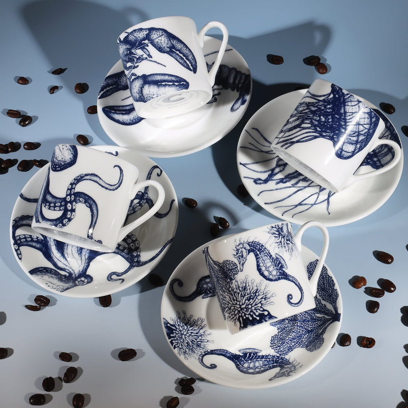 Four Bone China white espresso cups in hand drawn illustrations in our Octopus,Seahorse,Jellyfish and the Lobster designs in Navy with matching saucers.Saucers are arranged in a square with the cups lying on their sides on the saucers surrounded by coffee beans