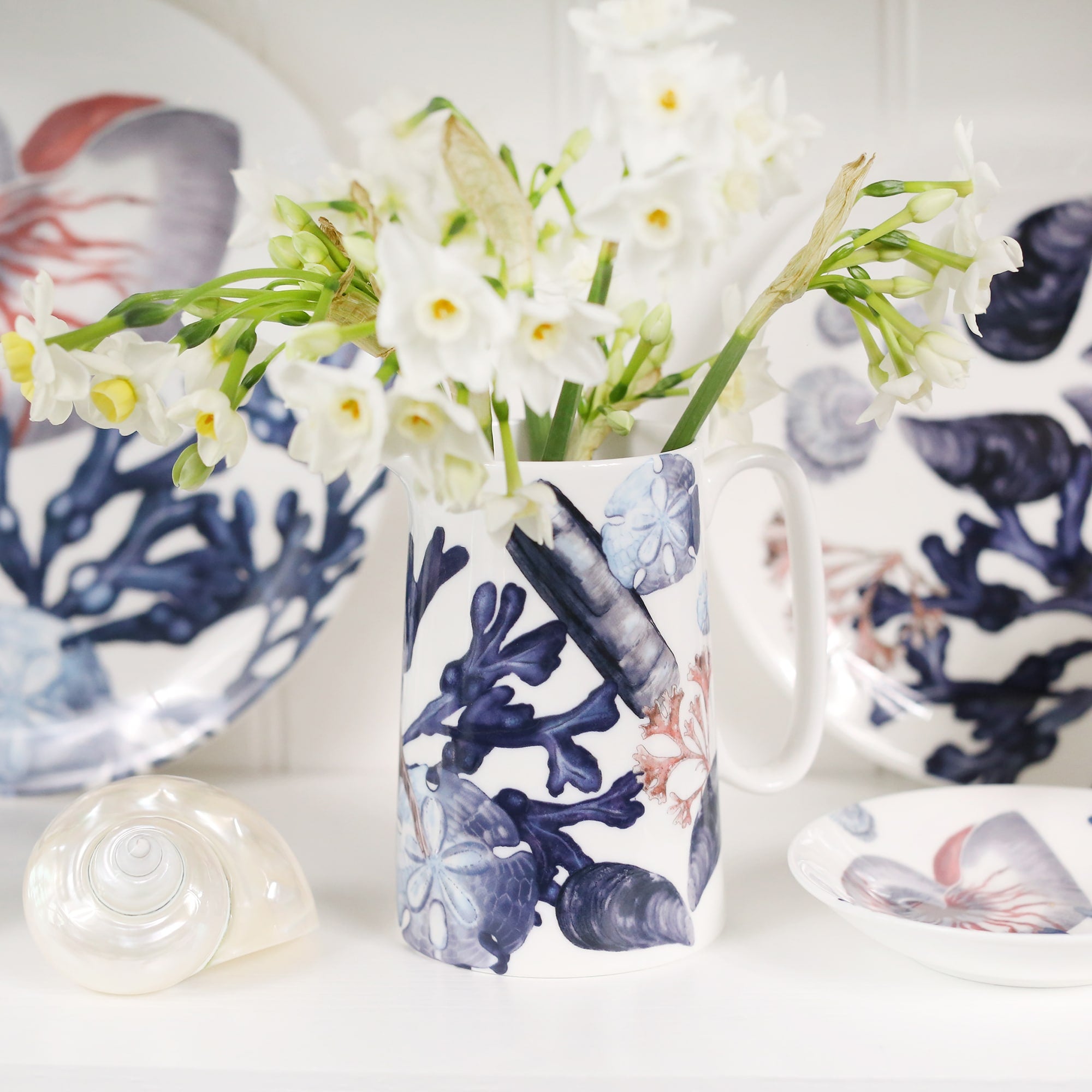 Medium size beachcomber jug showing shades of blue shells, seaweed and a starfish.In the jug are daffodils, in the background are matching beachcomber china