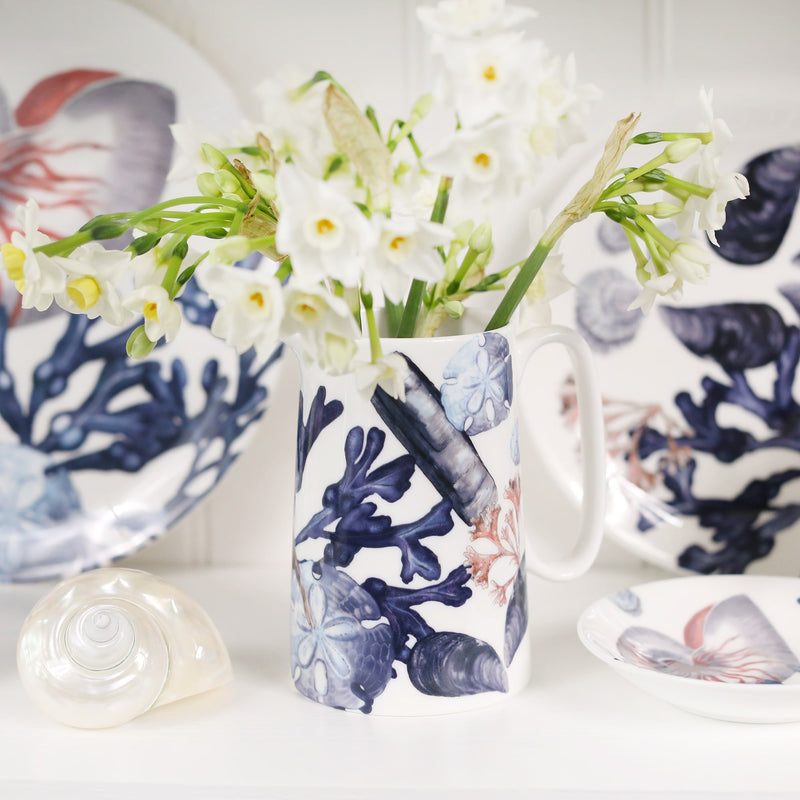 Medium size beachcomber jug showing shades of blue shells,seaweed and a starfish.In the jug are daffodils,in the background are matching beachcomber china
