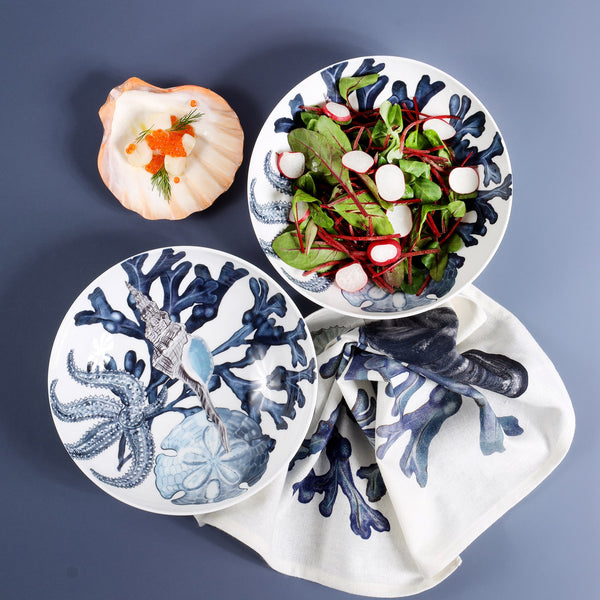 Two of our Beachcomber design pasta bowls,one of which has a radish salad in it and a beachcomber napkin and a scallop shell are also on the table 