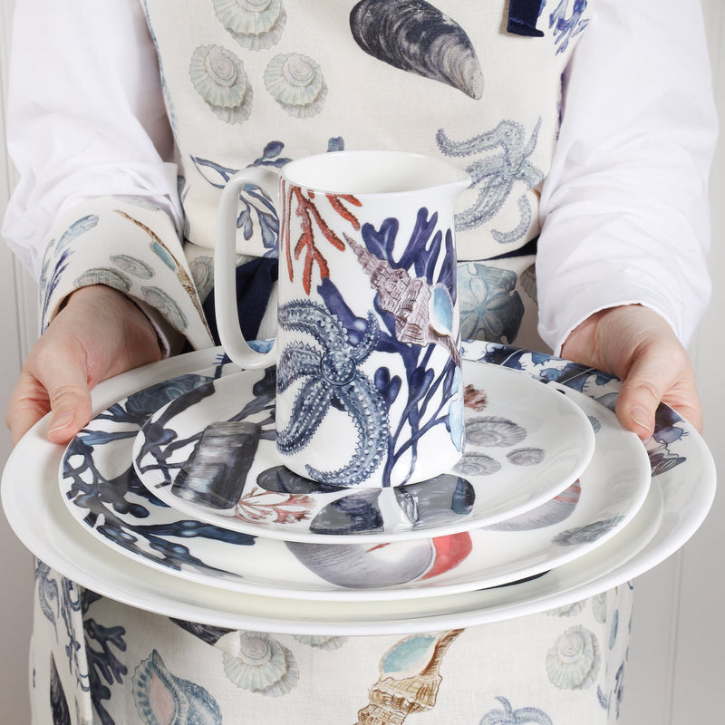 Bone china Beachcomber stack of side and dinner plates being offered towards you,held by someone wearing a beachcomber apron