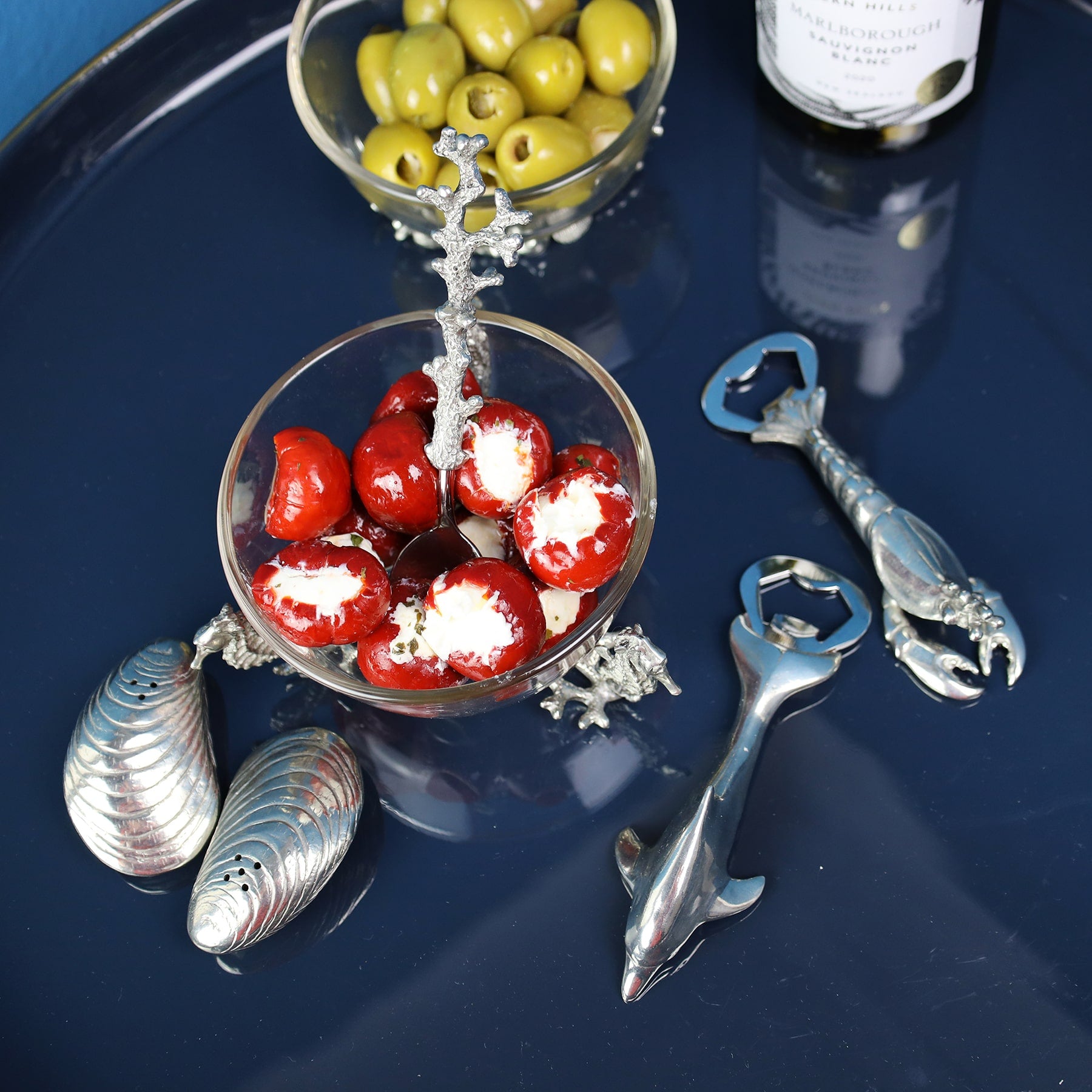 Pewter Dolphin and a Lobster shaped Bottle Opener placed on a table with a Mussel salt and pepper set and a glass bowl filled with olives