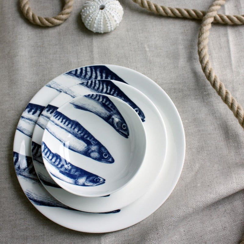 Bowl in Bone China in our Classic range in Navy and white in the Mackerel design stacked on a matching side plate and dinner plate placed on a tablecloth.On the table is a rope winding on the table and a shell