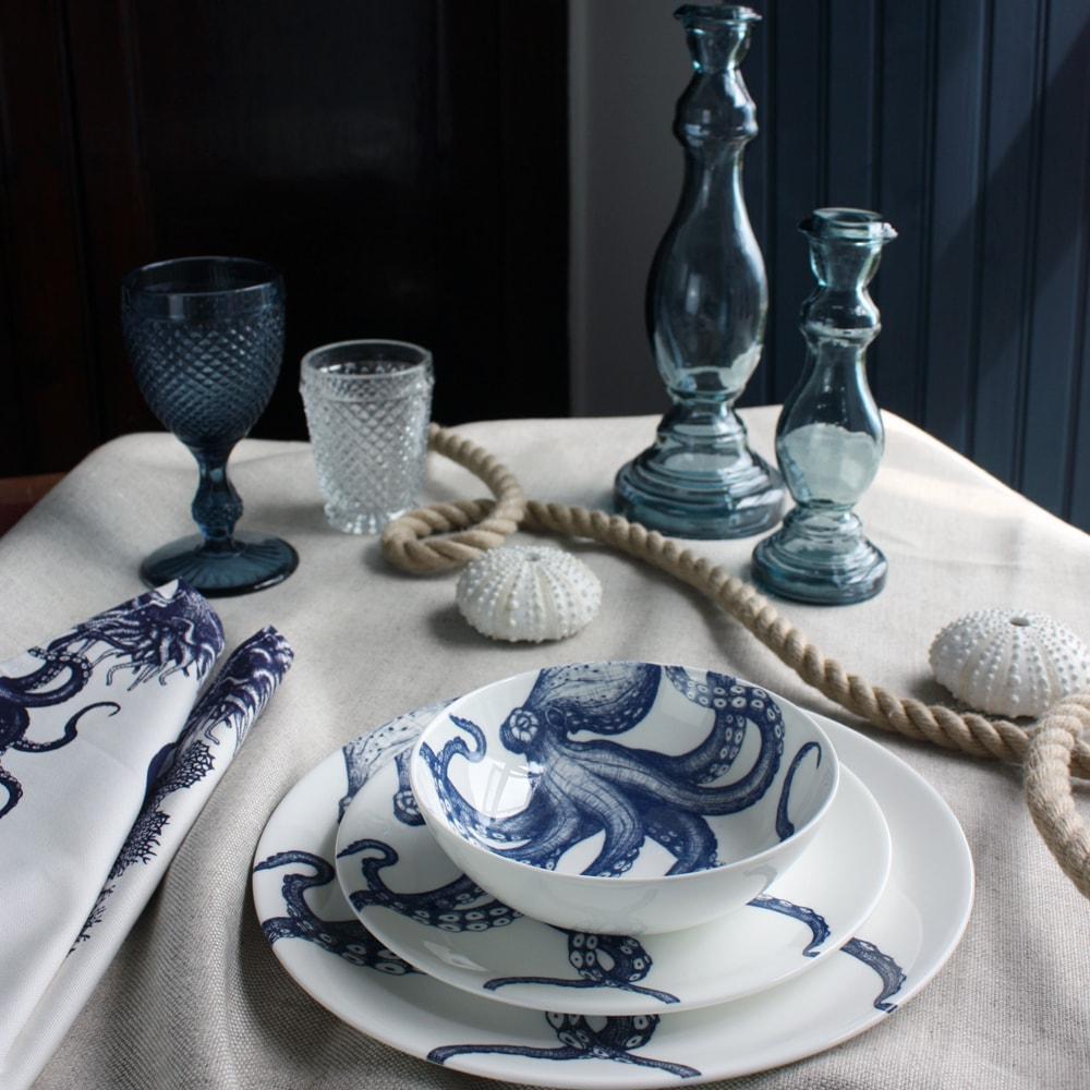 Bowl in Bone China in our Classic range in Navy and white in the Octopus design stacked on a matching side plate and dinner plate placed on a tablecloth.On the table is a matching napkins and a couple of glass candle holders 