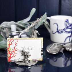 Pewter Coral & Seahorse Card Holder shown holding placecard and other pewter items in the background