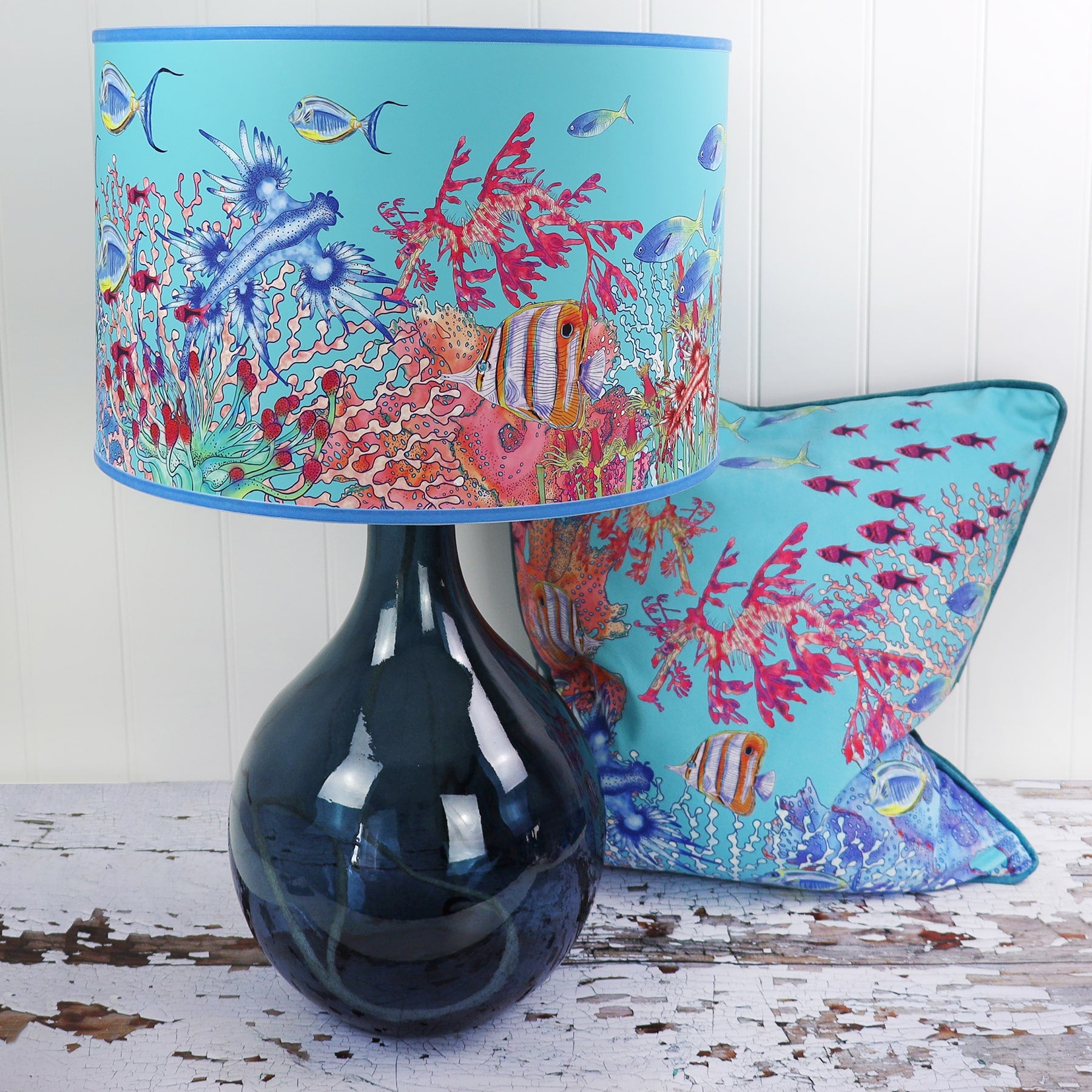 Coral Bay design lampshades in Turquoise on a glass lampbase in front of a Turquoise Coral Bay cushion
