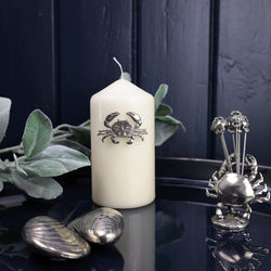 Pewter Crab Candle Pin decoration placed onto a thick white candle placed on a table next to other Pewter items