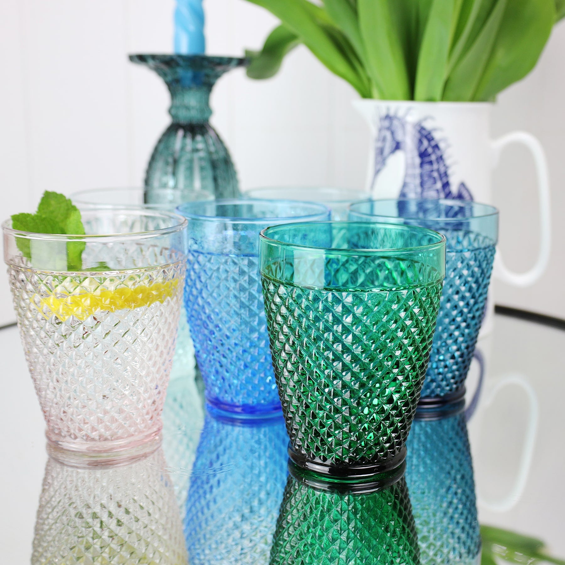 Lifestyle shot of four diamond cut tumblers on a mirror table,withaa seahorse jug in the background filled with tulips