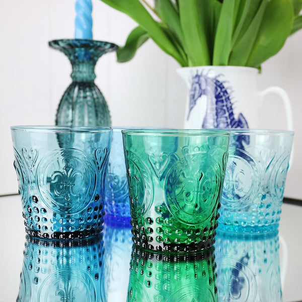 Cobalt Fleur de Lys Tumbler with other coloured glass tumblers on a mirror table with a seahorse jug filled with tulips