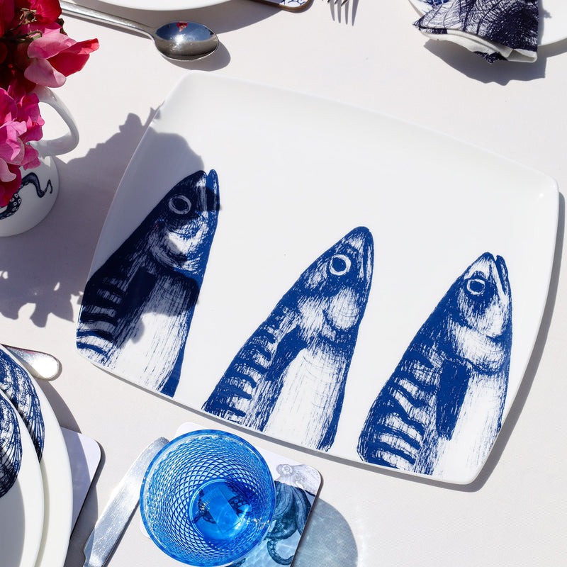 Platter in Bone China in our Classic range in Navy and white in the Mackerel design on a white tablecloth placed on a tablemat.In the background are other place settings in our classic designs