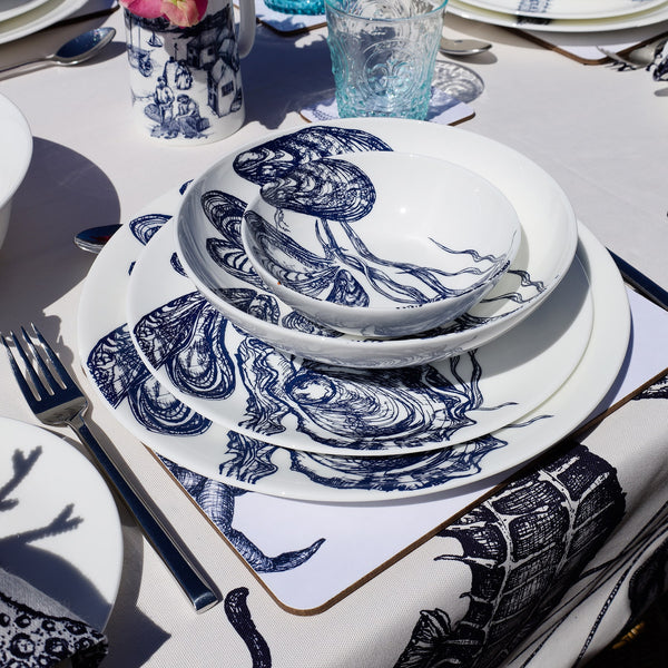 Outside Table setting with Large Mussel & Oyster plates,stacked with the bowls on a placemat,next to a coaster with a blue glass.