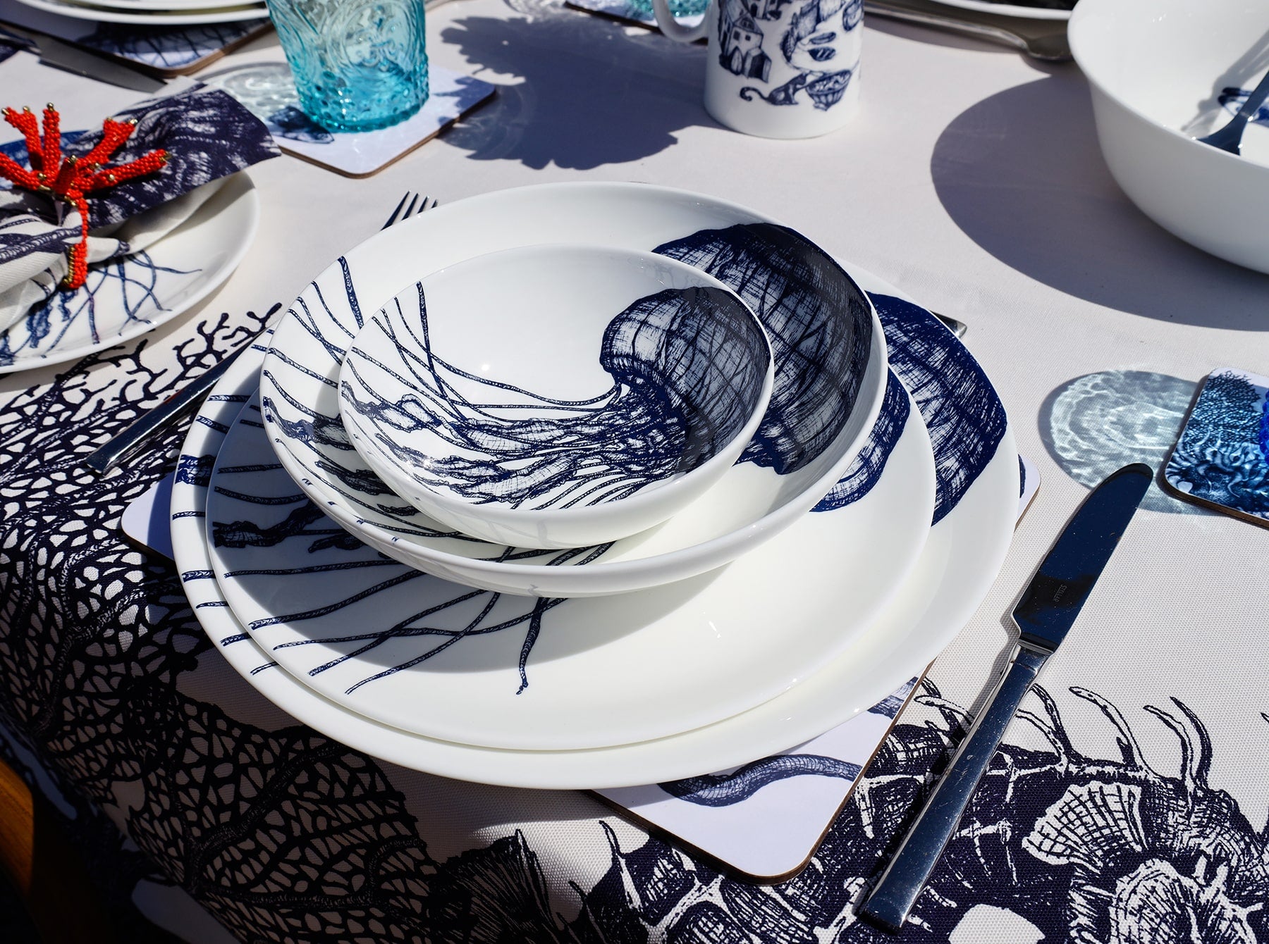 Outside Table setting with Large Jellyfish plates,stacked with the bowls on a placemat,next to a coaster with a blue glass.