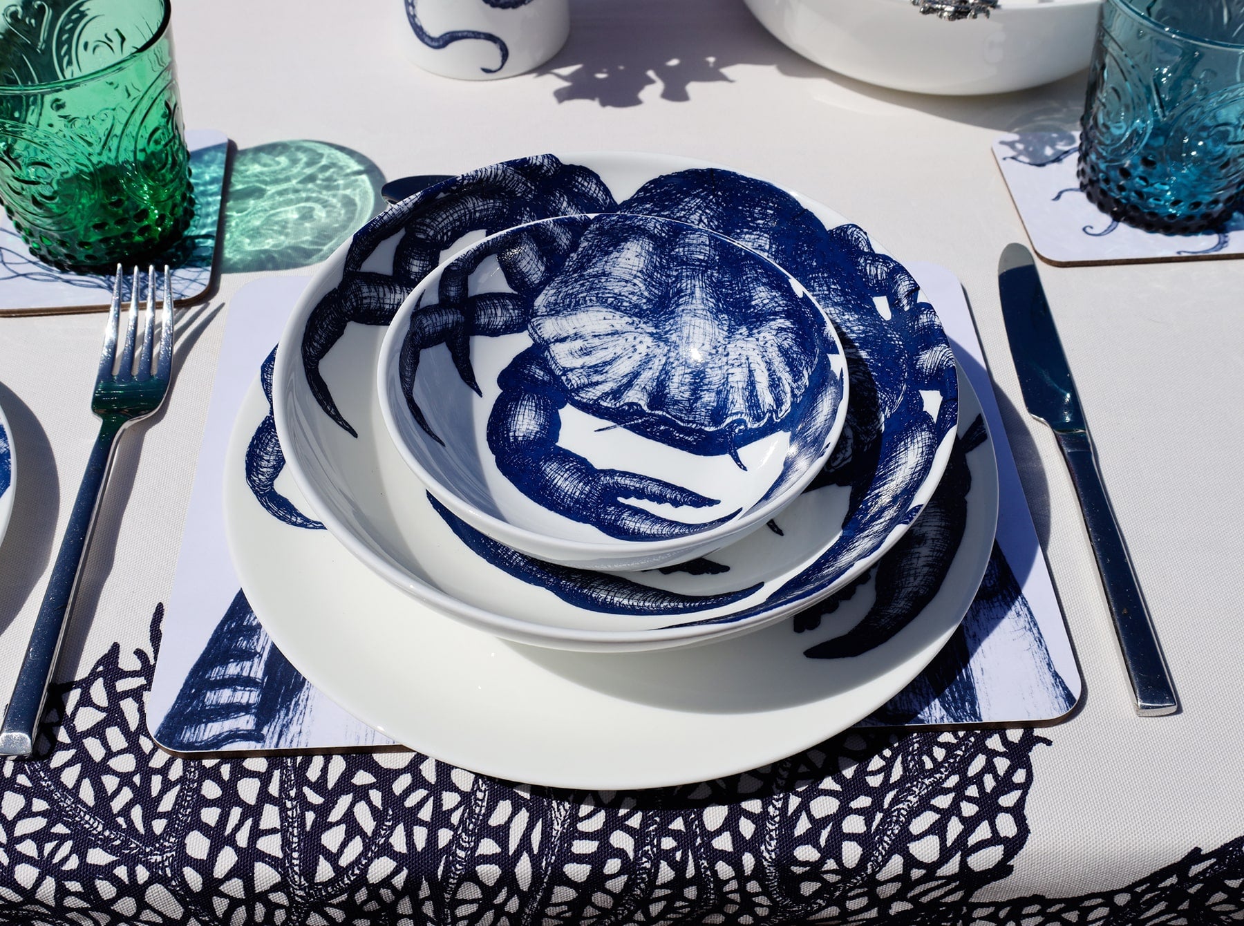 Outside Table setting with Large Crab plates,stacked with the bowls on a placemat,next to a coaster with a blue glass.