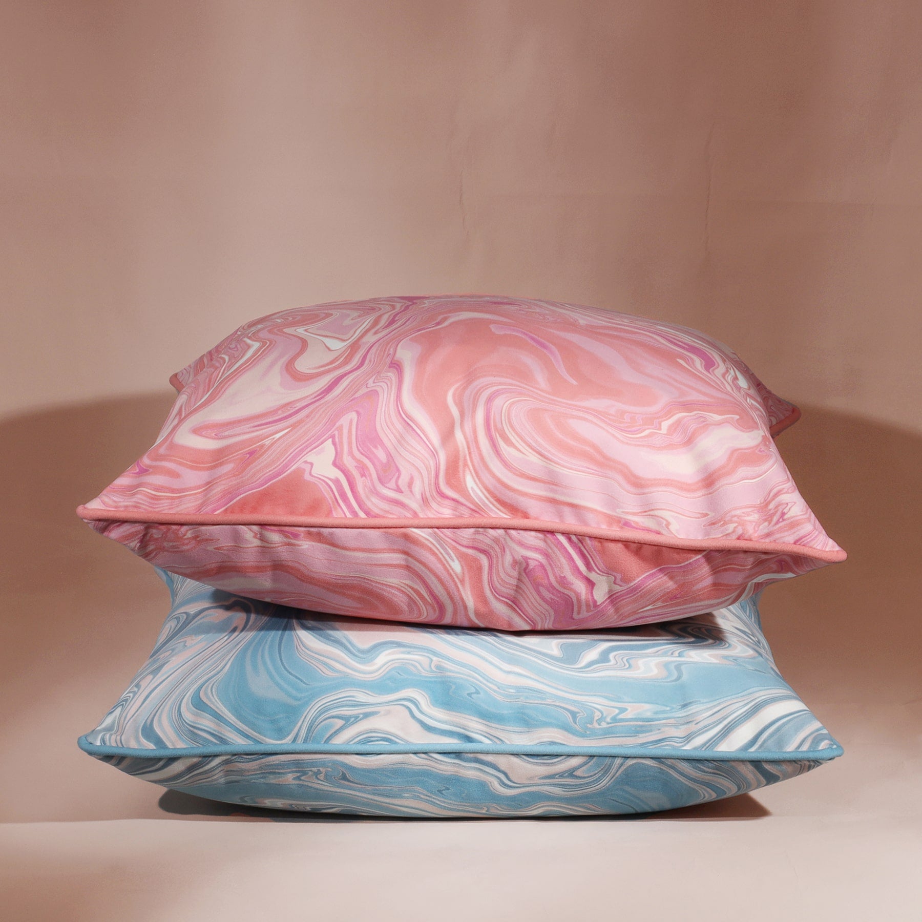Marble,swirl cushion in Sundowner colours in pinks/whites and coral placed on top of a similar design in blues.