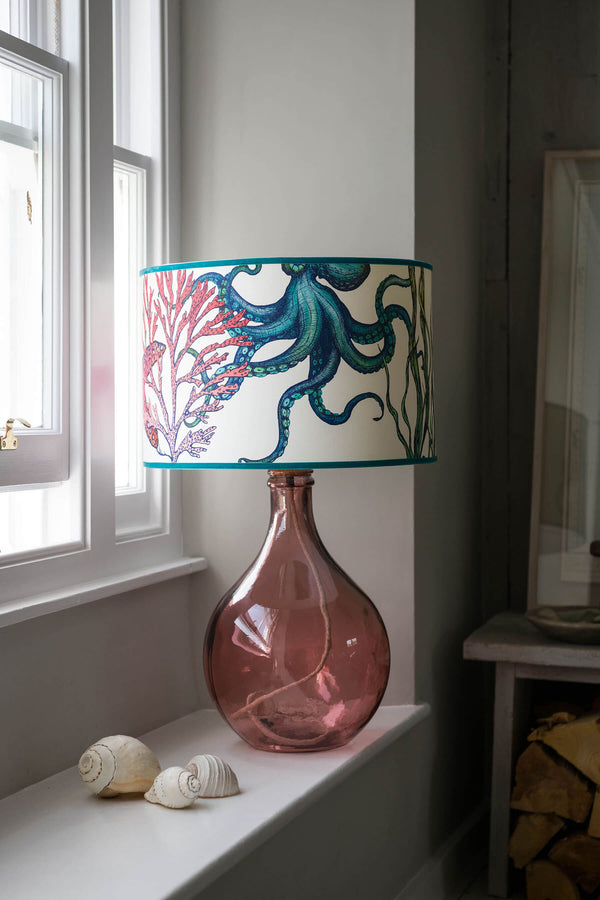 Rainbow Reef White Shade With Octopus,Seahorse,Starfish and Seaweed Design in bright colours on a pink lampbase on a window ledge.