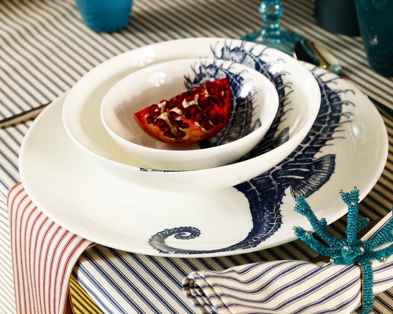 Bone China White plate with hand drawn illustrations of our Classic Seahorse in Navy stacked with the dinner plate,side plate and a bowl.Set in place setting with cutlery on a navy stripe tablecloth