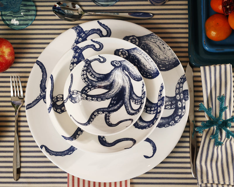 Aerial view of Bone China White plate with hand drawn illustrations of our Classic Octopus in Navy stacked with the dinner plate,side plate and a cereal bowl.Set in place setting with cutlery on a navy stripe tablecloth 