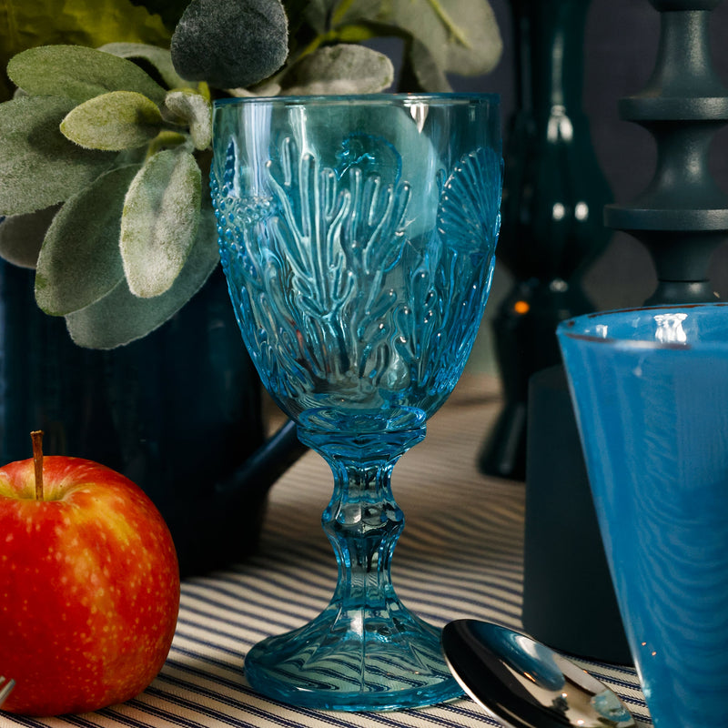 Teal coloured goblet with embossed sea creatures in the glass next to an apple on a table setting scene