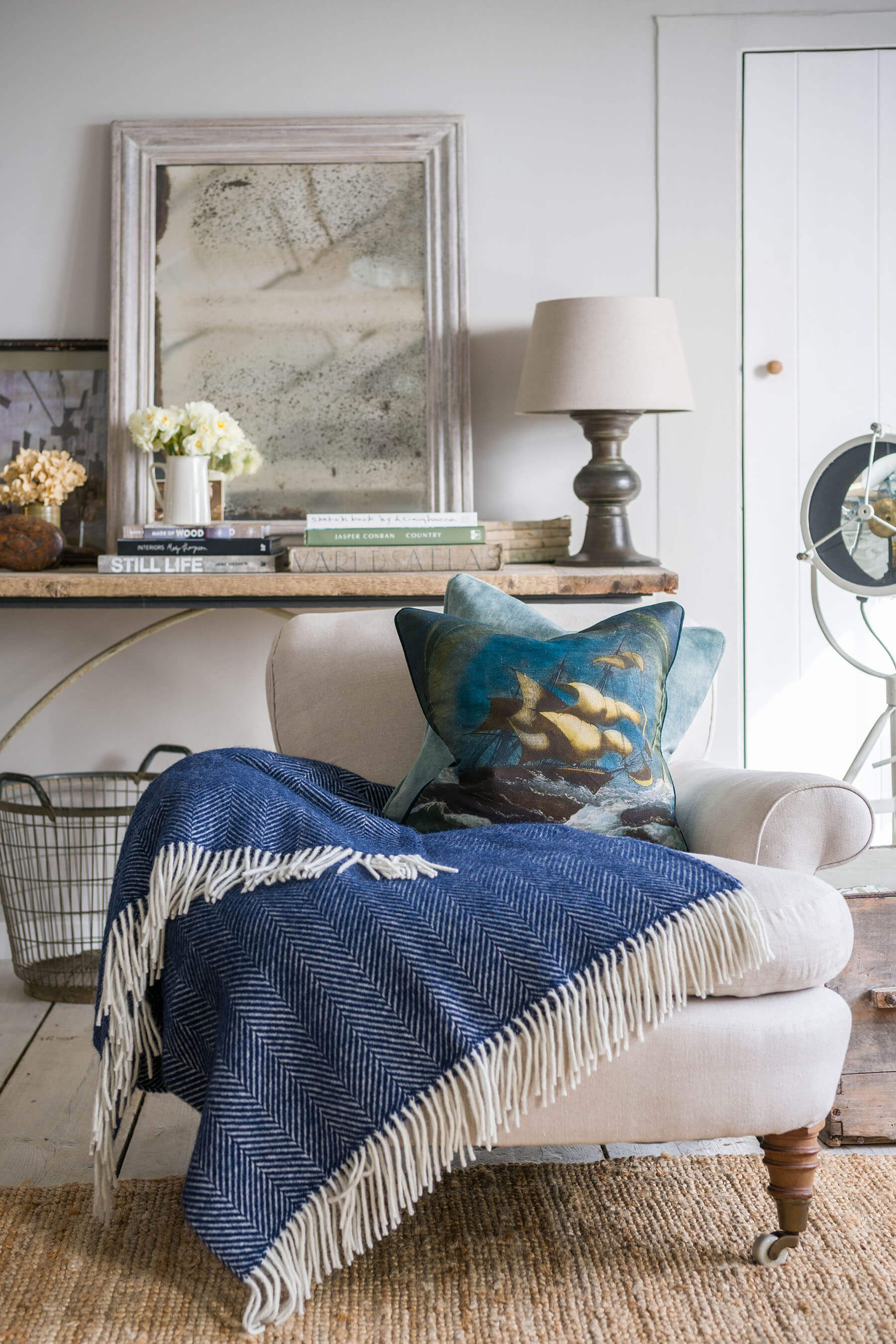 Tornado Cushion Cover ,scene of a billowing sailing ship in rough waters.placed on a cream seat with a navy throw,behind is a table with books and a mirror and vases