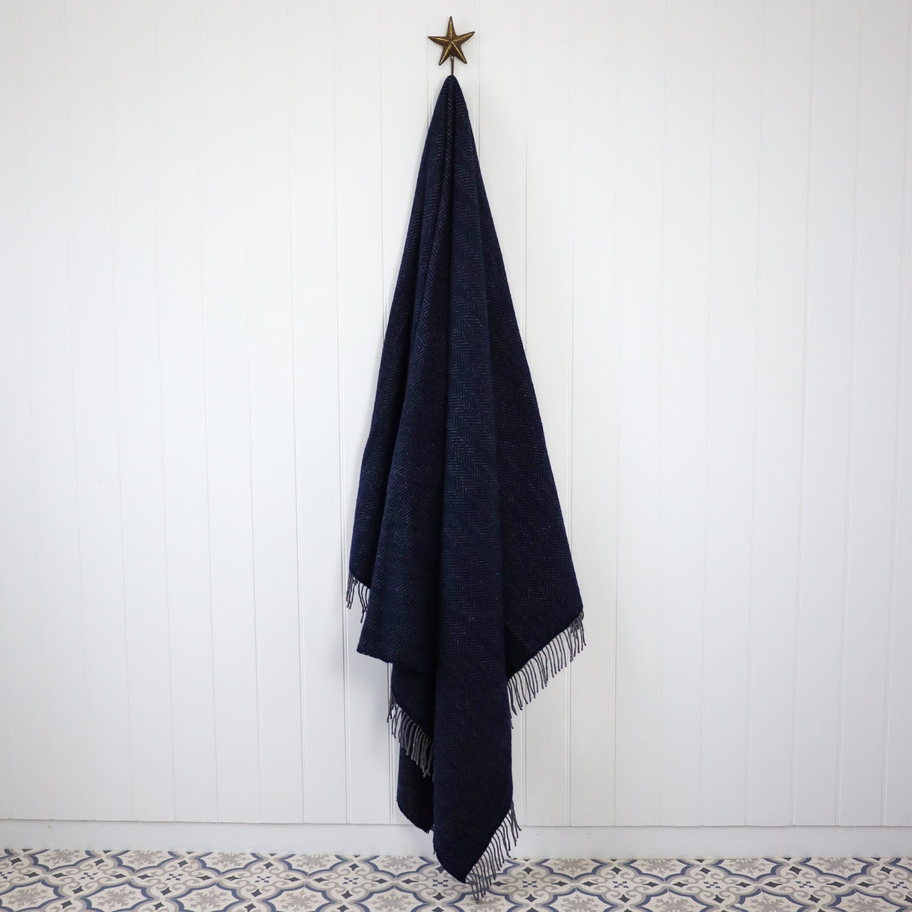 Cashmere Throw Dark Navy Herringbone hanging from a Starfish hook against a Tongue and Groove white wall