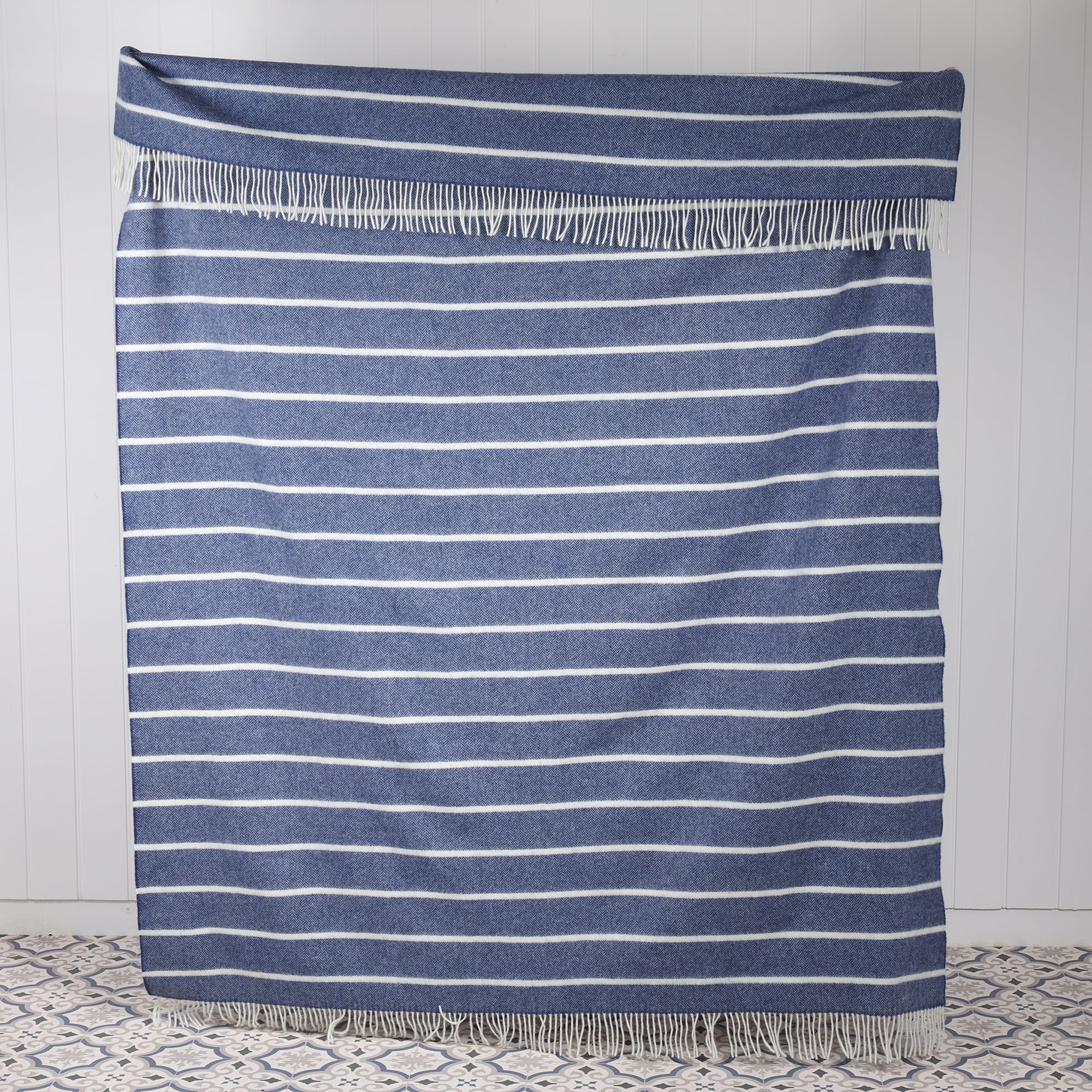 Lambswool Denim and White striped throw spread across against a white tongue and Grooved wall