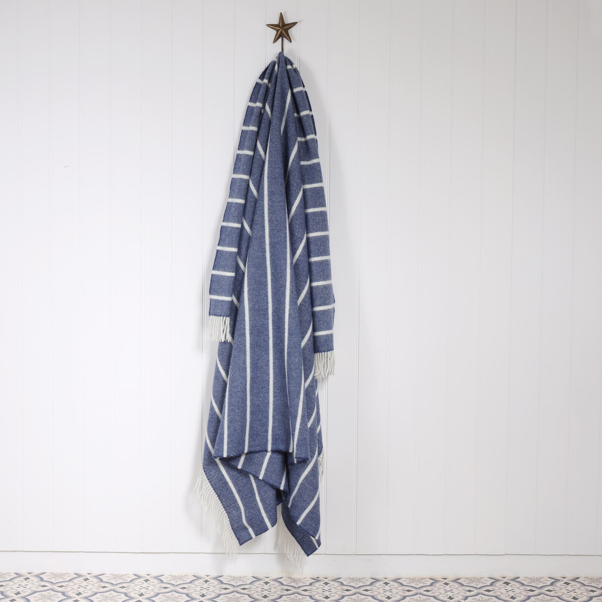 Lambswool Denim and White striped throw draped on a Starfish hook against a white tongue and Grooved wall